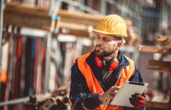 Construction site manager standing wearing safety vest and helmet,using his tablet at construction site.